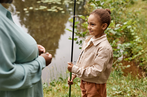 High angle portrait of black little girl holding fishing rod and smiling happily in nature