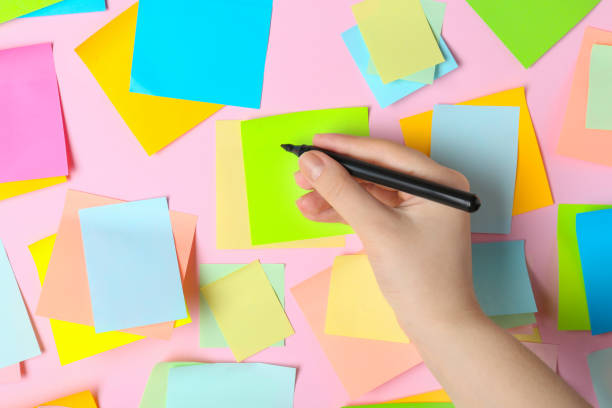 istock Woman writing on sticky note against pink background, top view 1470571600