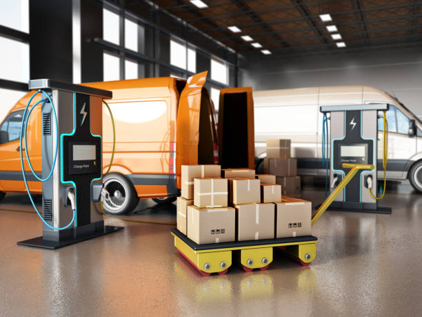 Electric commercial vehicles, industrial charging stations and stack of cargo boxes inside a distribution warehouse