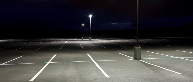 An empty parking lot sloping downhill at dusk lit with bright lights. 2.35:1 aspect ratio.