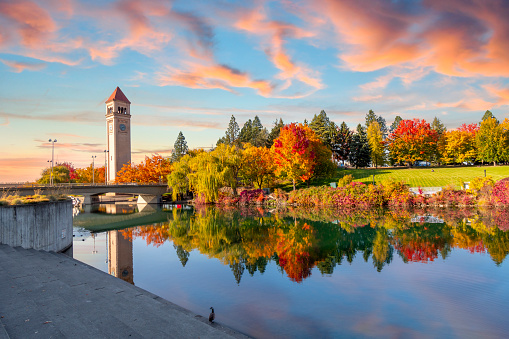 Vivid fall colors of red, orange, and yellow at the Spokane Washington Riverfront Park along the Spokane River with the Great Northern Clock Tower in view. Spokane is a city in eastern Washington state.