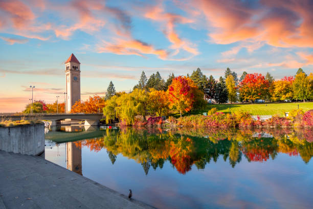 vivid fall colors of red, orange, and yellow at the spokane washington riverfront park along the spokane river with the great northern clock tower in view. - water lake reflection tranquil scene imagens e fotografias de stock