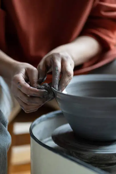 Artisan woman hands shaping deep plate made of natural clay placed on spinning potter wheel in workshop. Closeup of dirty fingers of sculptor girl sculpting home furnishings for sale at handmade fair