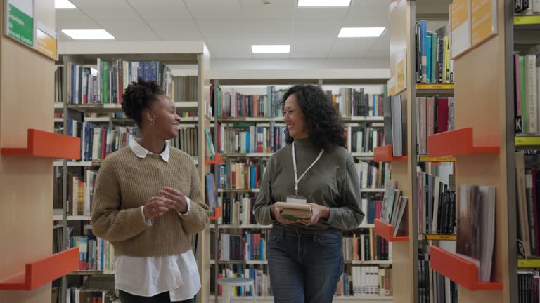 Mature Hispanic Librarian Helping A Young Adult Black Female Student