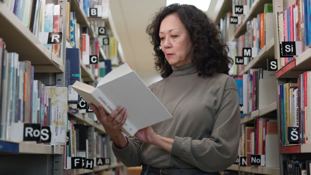 Mid Adult Hispanic Female Reading A Book  Standing In A Library