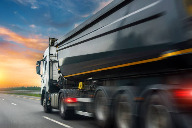 istock Truck huge dump trailer with bulk cargo drives fast spinning tire rubber wheels along the evening highway at dusk sunset with motion blur effect. 1470582575