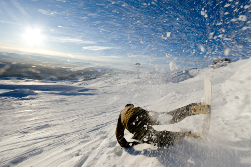 Snowboarder falling after a jump and makes a great cascade of snow.