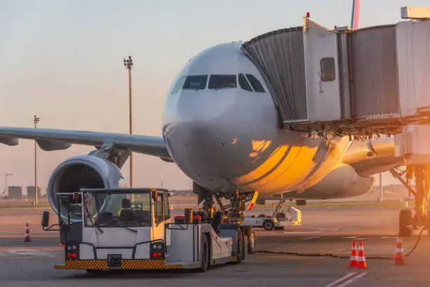 Aircraft is attached to the terminal gangway of the airport building preparation for towing and launch flight in the evening at sunset