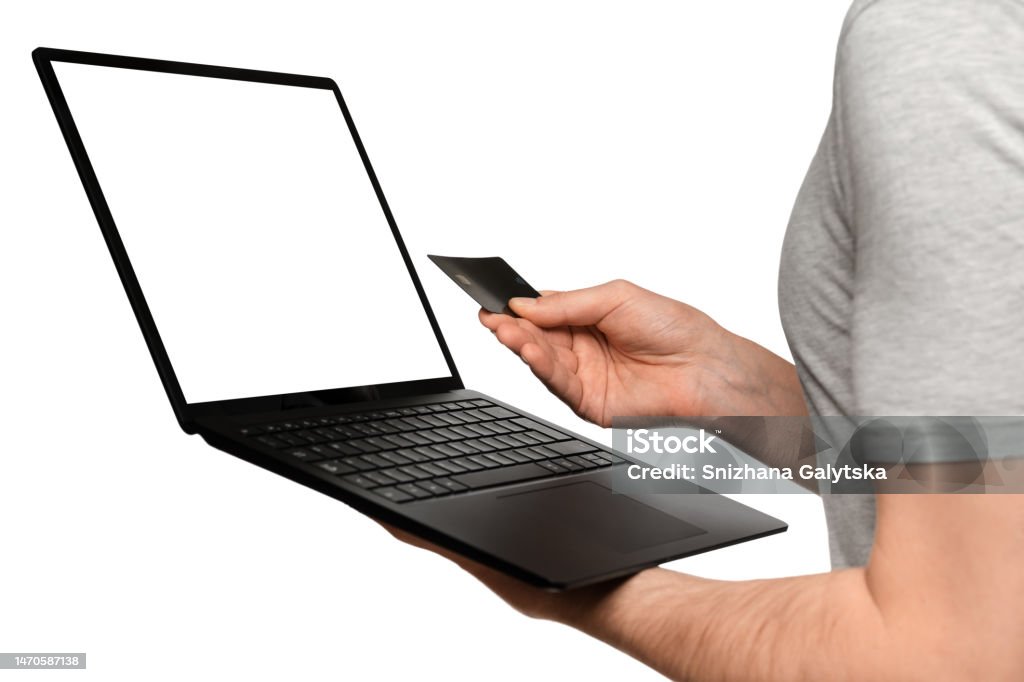 A man in a T-shirt holds a laptop, an ultrabook and a bank card with his second hand, makes an online purchase. Adult Stock Photo