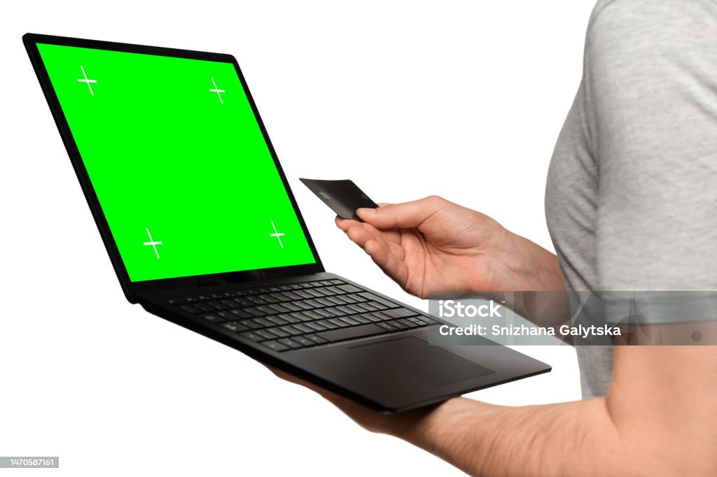 A man in a T-shirt holds a laptop, an ultrabook and a bank card with his second hand, makes an online purchase. Adult Stock Photo