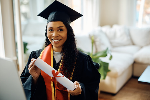 Happy African American college graduate holding her diploma while looking at camera.