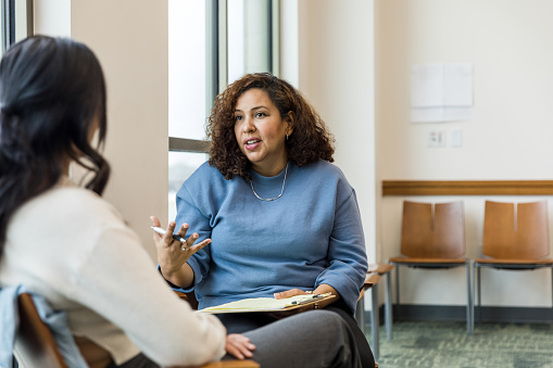 The female therapist gestures while she talks to the unrecognizeable woman about some strategies she can use at work to deescalate tough situations.