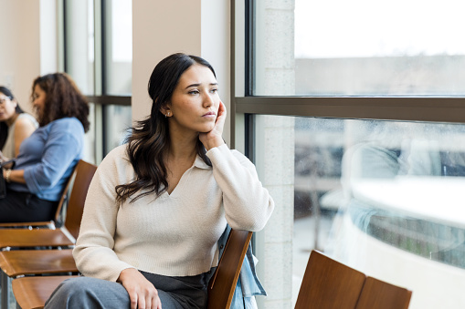 The sad young woman sits in the waiting room and waits for her appointment with the therapist.