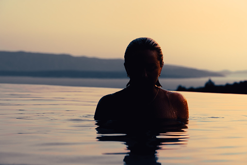 Girl at sunset in the pool. In the background, the sea and mountains.