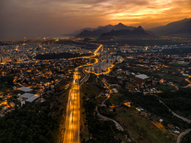 aerial view Antalya city at night time. We see the highway in the front, the city in the back, and the sea and mountains in the back. Long exposure shot. Drone shot.