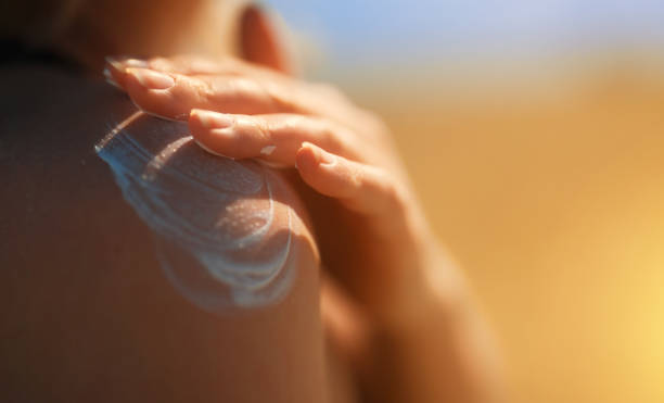 mujer aplicando crema bloqueador solar en su hombro. - crema de sol fotografías e imágenes de stock
