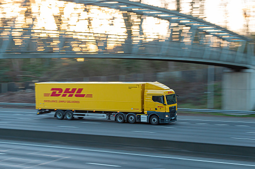 Chorleywood, UK - February 25, 2023: Yellow lorry belonging to German courier company DHL in moton on British motorway M25