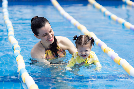 Mother and daughter in the pool, teaching baby girl to swim