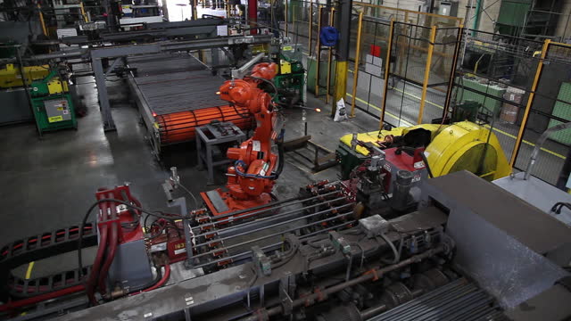 A robotic arm moves steel rods in an industrial factory assembly line