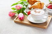 Happy mother's day, beautiful breakfast, lunch with cup of coffee (cappuccino) fresh croissants, strawberries on tray, bouquet of tulips as gift.