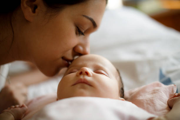 Madre che bacia il suo neonato addormentato - foto stock