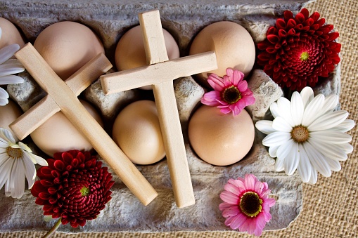 An easter background of eggs in an egg box with a crucifix cross and flowers.