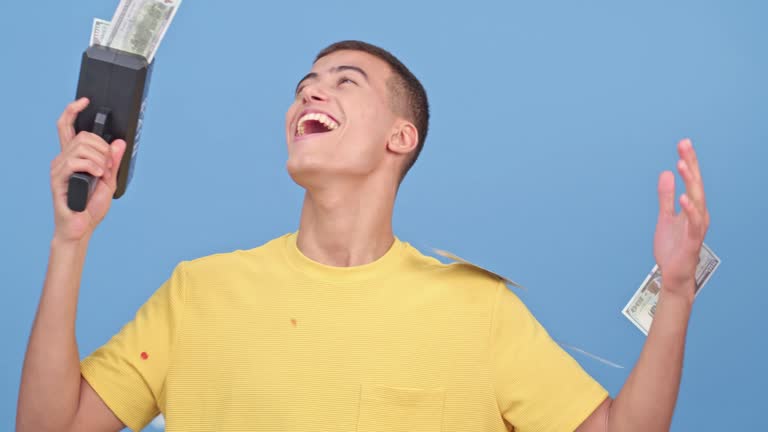 Lottery, win and man with a money gun for celebration isolated on a blue background in studio. Finance, success and person with a machine to rain cash after winning a competition, bonus or jackpot