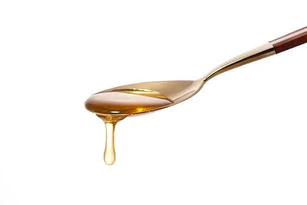 honey dripping from a golden teaspoon on a white background
