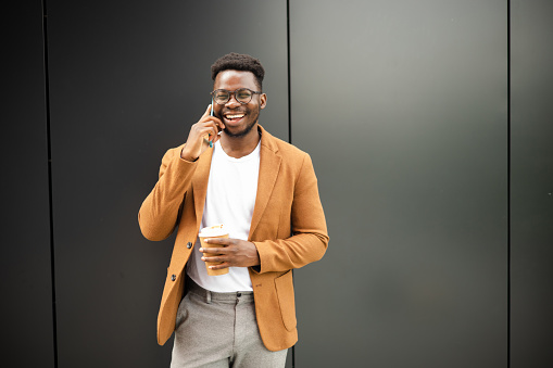 Portrait of a young African American businessman on a coffee break talking on mobile phone outdoors