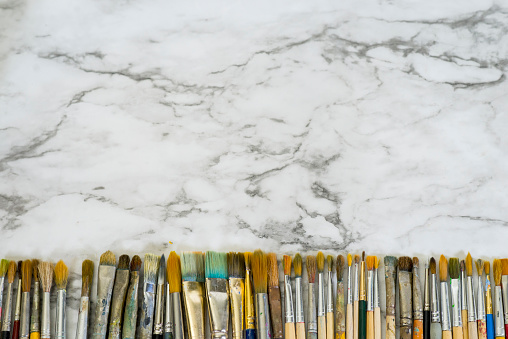 Horizontal straight line of assorted artist's paintbrushes of different sizes and types lined up against a bright clean marble background.