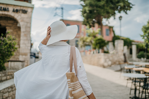 Unrecognizable mature woman carrying a bag is walking on the small town street, she is on vacation in Greece.