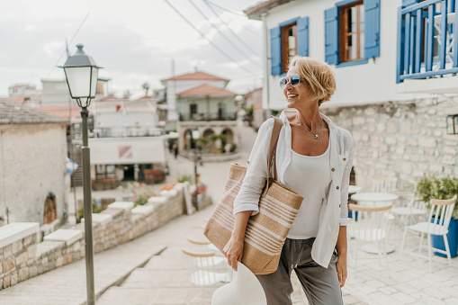 Mature woman carrying a bag is walking on the small town streets, she is on vacation in Greece.