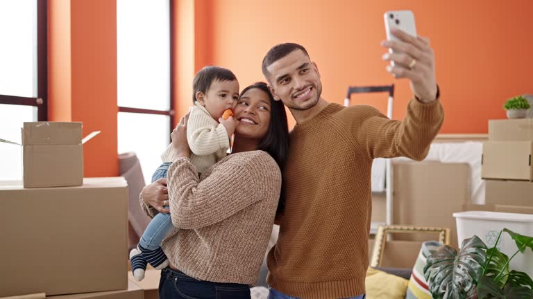 Couple and son hugging each other make selfie by smartphone at new home