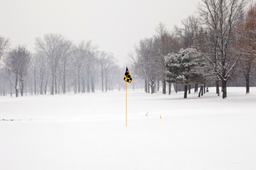 looking back from the hole at a snow covered golf course as more snow is falling lightly
