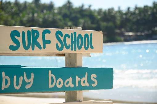 Surf school and lessons sign on tropical beach with big wave.