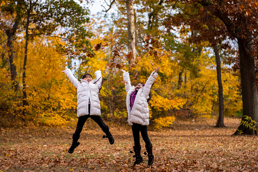 Two young asian girls tossing leaves in the air