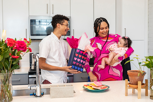 Young married couple celebrating Valentine's Day with there new born by giving gifts and making handmade cards