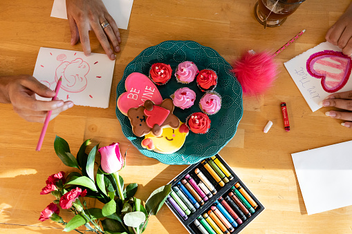 Young married couple celebrating Valentine's Day with there new born by giving gifts and making handmade cards