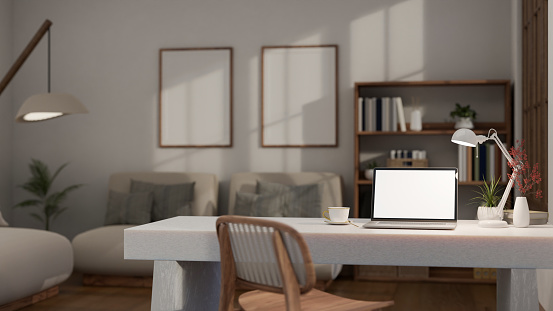 Interior design of modern workspace in contemporary and cozy living room, laptop white screen mockup, table lamp, and decor on white stone table. 3d render, 3d illustration