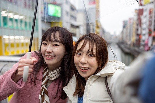 Female friends talking selfie photos on bridge in city - looking at camera