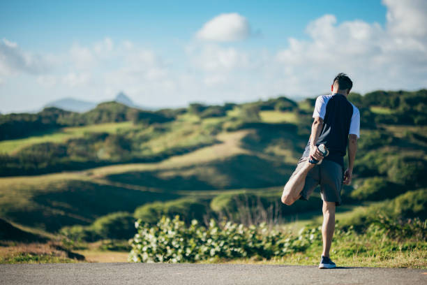 After/before jogging in a natural park, the Asian male is stretching his muscles while facing the vast natural scenery, in order to maintain optimal muscle condition and tone.