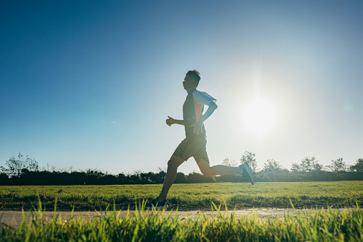 The Asian male athlete is practicing running outdoors with precise coordination of breathing and speed, aiming to improve his cardiovascular function, maintain physical health, and enhance his competitiveness.
