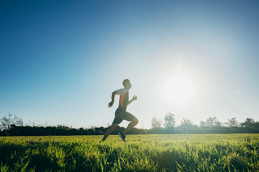The Asian male athlete is practicing running outdoors with precise coordination of breathing and speed, aiming to improve his cardiovascular function, maintain physical health, and enhance his competitiveness.