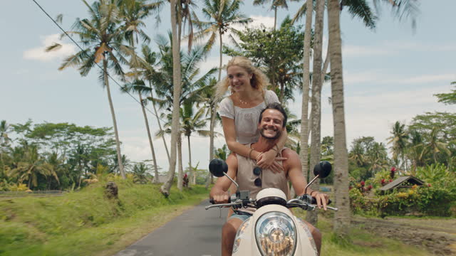 travel couple riding scooter on tropical island happy woman celebrating with arms raised enjoying fun vacation road trip with boyfriend on motorcycle ride