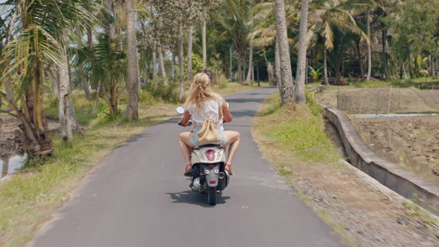 tourist couple riding motorbike on tropical island happy woman celebrating freedom with arms raised enjoying vacation road trip with boyfriend on motorcycle ride rear view