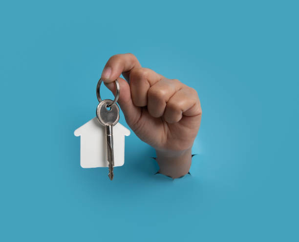 istock Female hand holding house key breaks through blue paper background. 1470654311