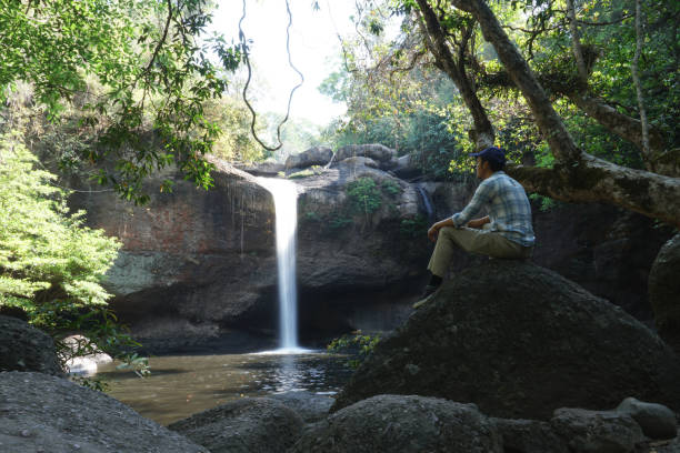 istock asian men sitting on the rock with water fall background. 1470654879