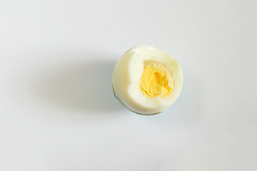 a bite of a boiled egg in the shell lies on a white background