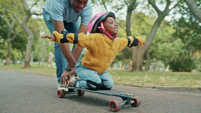 Black family, father and girl child with skateboard, pushing and plane game in street with bonding. Dad, daughter and freedom at park, playing and love with learning, helmet and safety in nature