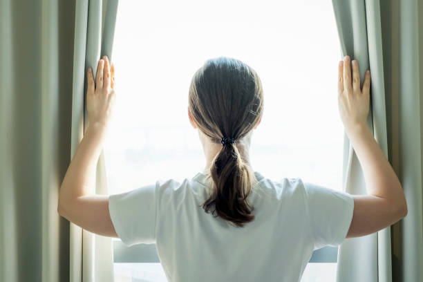 istock Young woman stands at window and opens curtains back view. 1470666776